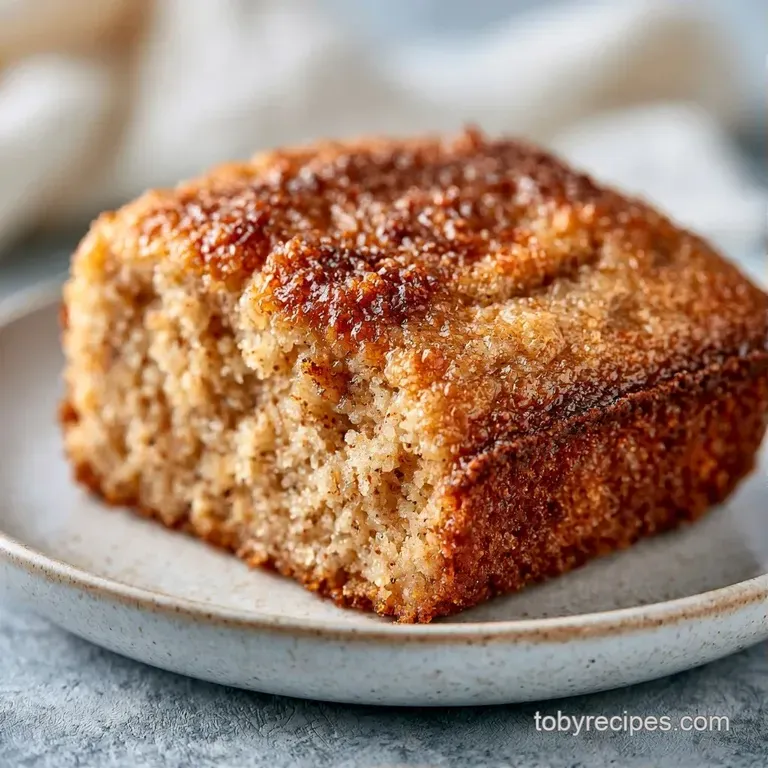 A thick slice of moist cake with a crumbly cinnamon topping on a white plate beside a steaming cup of black coffee.